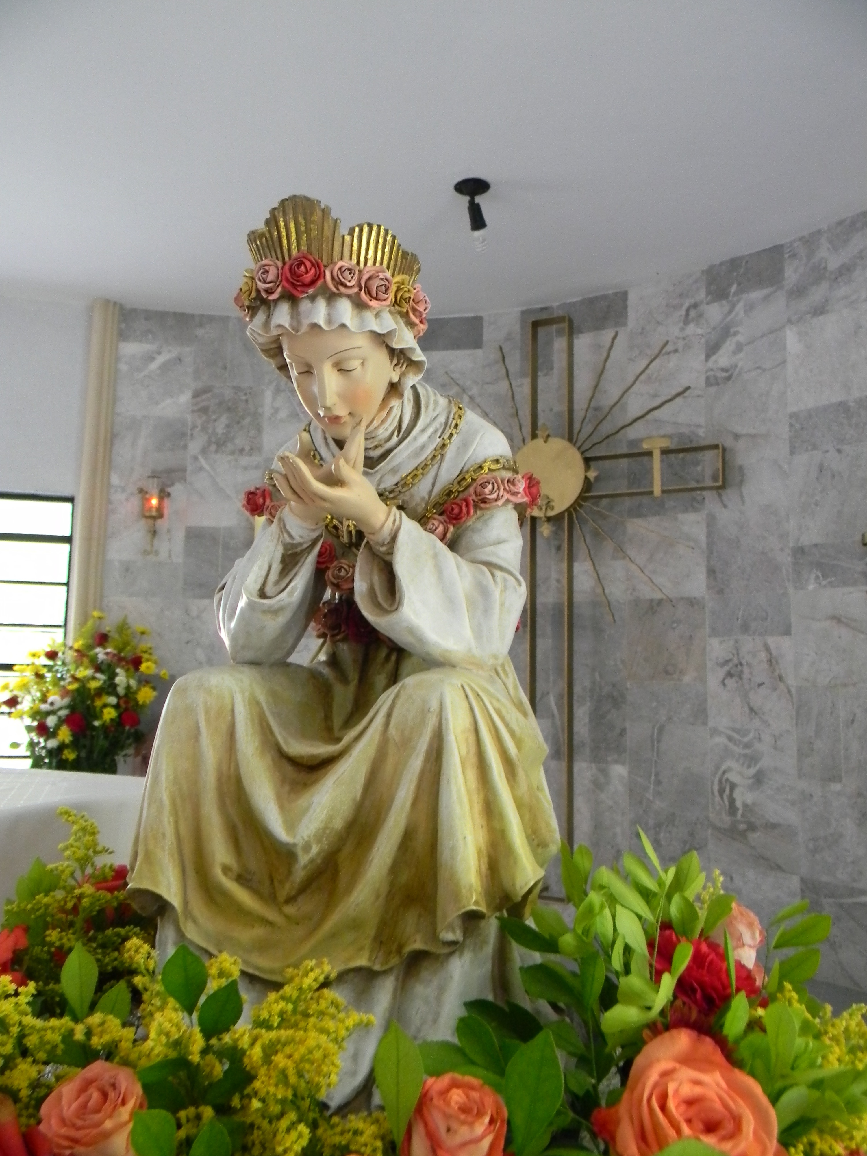 Estatua de la Virgen con una corona de rosas, rodeada de flores en la capilla